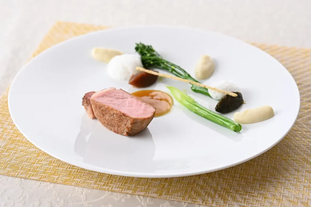 フランス産ビゴール豚のロティ 蕗の薹のキャラメリゼと山椒のクルスティアン 新玉ねぎの甘美なピュレ デーツと黒にんにくのコンフィチュールを添えて（イメージ）